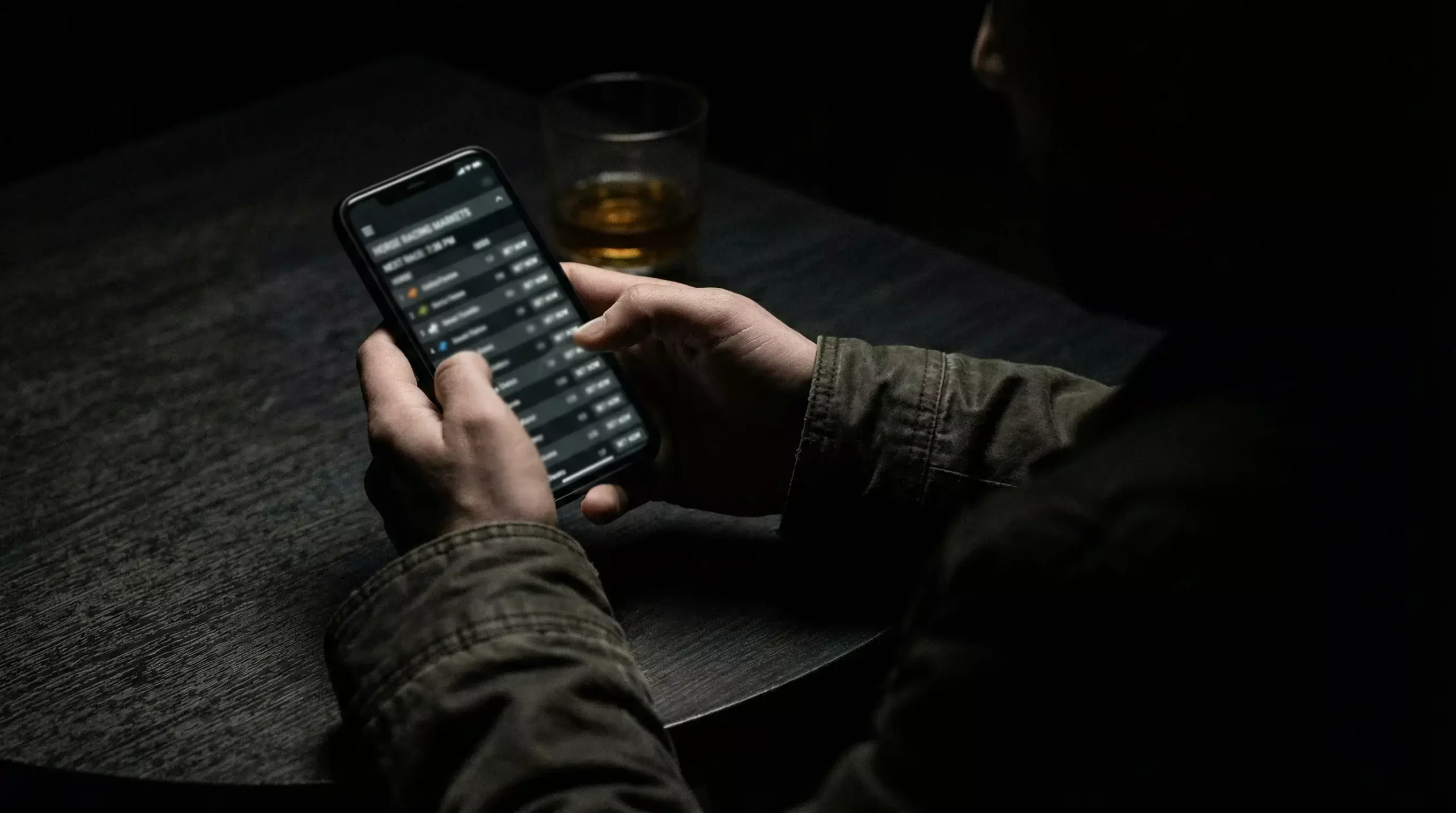 Person using smartphone with unlicensed betting site in shadowy setting